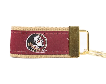May include: A tan and maroon key chain with a gold key ring. The maroon section features a Seminole State University logo with a Native American mascot.