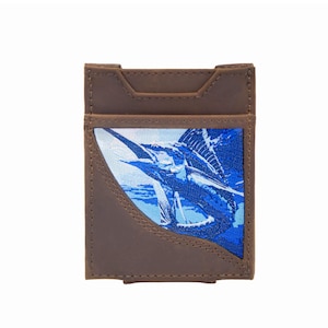 May include: Brown leather card holder featuring a blue marlin fish design. The card holder is rectangular with a curved front cutout and a top slot. The marlin is shown in blue hues against a white and blue backdrop.