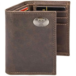 May include: Brown leather wallet with a silver emblem. The wallet is open, revealing card slots and a bill compartment. The emblem features a stylized letter "T". The leather has a distressed appearance.
