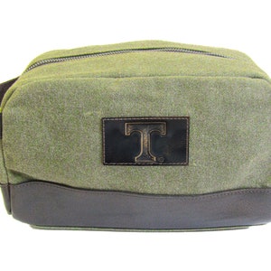 Neceser Dopp para artículos de tocador para hombre Tennessee Vols. Lona encerada de color verde oliva con ribete de cuero de plena flor bruñido marrón. Logotipo de parche grabado.
