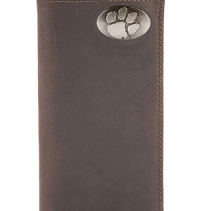 Puede incluir: Cartera de cuero marrón con un emblema plateado de huella de pata. La cartera es rectangular y tiene un diseño plegable. Las costuras son visibles a lo largo de los bordes.