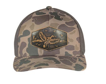 Mallard Old School Camo Trucker Hat. Hand Burnished Full Grain Leather Patch. 5-Panel Richardson 112 Snapback Cap. Stitched Duck Patch.