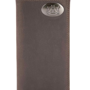 Puede incluir: Una cartera de cuero marrón con un emblema plateado con la letra "A" y la palabra "AUBURN". La cartera es rectangular y tiene un borde cosido. Es una cartera de dos pliegues.