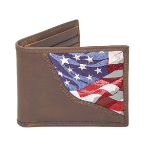 Puede incluir: Cartera de cuero marrón de dos pliegues con una sección que presenta la bandera estadounidense. El diseño de la bandera incorpora rayas rojas y blancas con estrellas azules y blancas. La cartera está abierta, revelando ranuras para tarjetas.