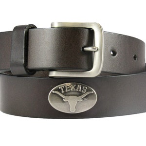 May include: A brown leather belt with a silver buckle and a silver oval-shaped emblem with the word "TEXAS" and a longhorn steer silhouette.