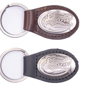 May include: Two keyrings featuring a silver alligator emblem on a leather backing. One has a brown leather backing, the other black. Both have a silver key ring. The keyrings are suitable for keys.