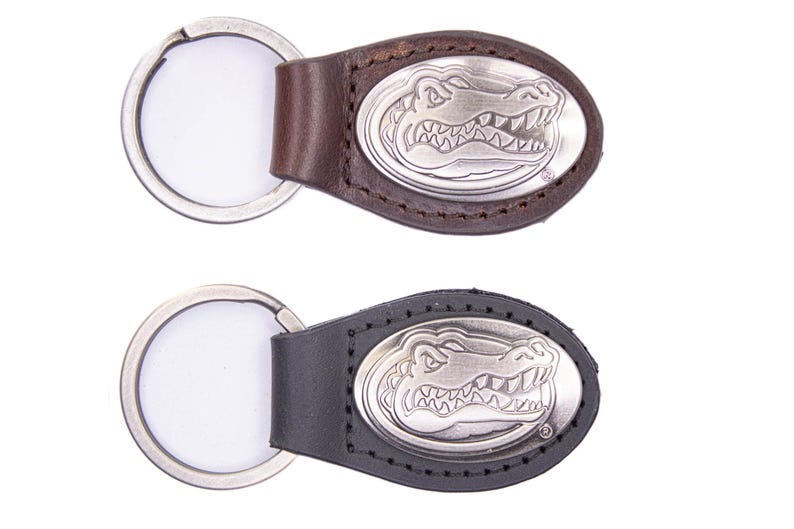 May include: Two keychains with a silver alligator emblem on a leather backing. One keychain has a brown leather backing, and the other has a black leather backing. Both keychains have a silver key ring.