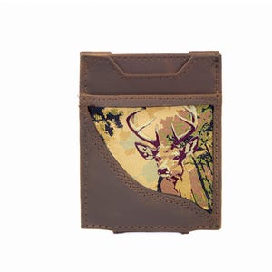 Puede incluir: Un tarjetero de cuero marrón con una ilustración de ciervo en tonos marrones, verdes y beige. El tarjetero tiene forma rectangular con un bolsillo curvo y una ranura para facilitar el acceso.