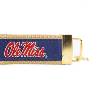 May include: A tan and blue key chain with a gold clasp. The key chain has the words "Ole Miss" embroidered in red.