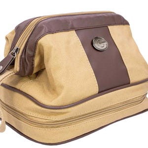 May include: Tan and brown toiletry bag with a zippered closure and a handle. The bag features a brown leather accent and a metal emblem with the letter "G". The bag is made of canvas material.