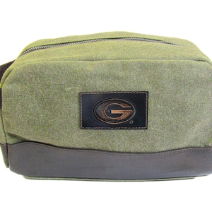 Könnte beinhalten: Grüne Reisetasche aus Canvas mit braunem Lederbesatz und einem braunen Lederflicken mit einem goldenen "G"-Logo.