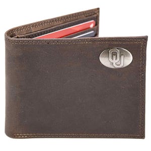 Puede incluir: Cartera de cuero marrón con un emblema ovalado plateado. La cartera está abierta, revelando tarjetas de crédito. Las costuras son visibles en los bordes. La cartera mide aproximadamente 11,4 cm de ancho y 8,9 cm de alto.