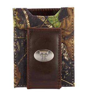 May include: A camouflage-patterned wallet with a dark brown leather money clip. The money clip features a silver-colored oval emblem with a stylized "T" in the center. The wallet is designed to hold cards and cash.