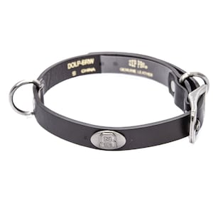 May include: Black leather dog collar with a silver-colored buckle and a metal ring for leash attachment. The collar has a small, oval metal emblem with a logo. The text "DOLP-BRN" and "GENUINE LEATHER" are visible.