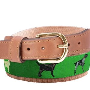 May include: A tan leather belt with a gold-colored buckle. The belt features a green fabric band with embroidered black dog silhouettes. The belt is designed for casual wear and has a classic style.