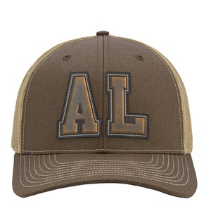 May include: A brown baseball cap with a mesh back and a curved brim. The front panel features the letters AL in a block font with a dark outline and a metallic, weathered copper-toned finish. The cap includes tonal stitching along the brim.