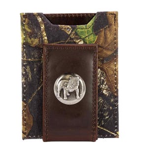 Puede incluir: Una cartera con estampado de camuflaje con un clip para billetes de cuero marrón oscuro. El clip para billetes presenta un emblema plateado de un bulldog. La cartera está diseñada para guardar tarjetas y efectivo.