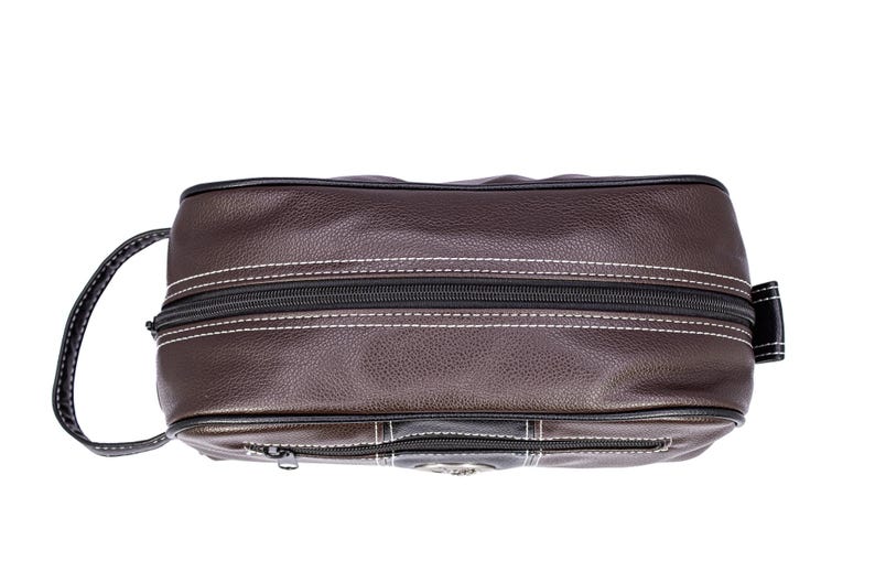 Puede incluir: Un neceser de cuero marr&oacute;n con cremallera negra y costuras blancas. La bolsa tiene un asa en un lado y un peque&ntilde;o bolsillo con cremallera en la parte delantera. La bolsa es de forma rectangular.