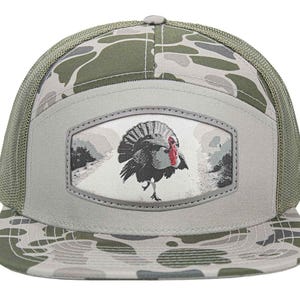May include: A camouflage-patterned trucker hat with a gray front panel featuring a turkey illustration. The hat has a mesh back and a curved brim. The turkey is depicted in a detailed, realistic style, with a red wattle and a gray and white background.