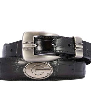 May include: Black leather belt with a silver-toned buckle and a matching belt loop. The belt features a textured pattern and a silver oval emblem with the letter "G".