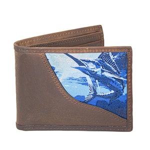 Puede incluir: Cartera de cuero marrón de dos pliegues con un diseño de pez marlín azul y blanco. La cartera tiene un borde cosido y un panel azul contrastante con la ilustración del pez. La cartera está abierta, mostrando las ranuras internas para tarjetas.