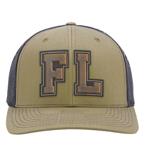May include: An olive green baseball cap with a dark charcoal mesh back and a curved brim. The front panel features the letters FL in a large, block-style font with a dark, weathered brown texture and a white stitched outline on the edges.