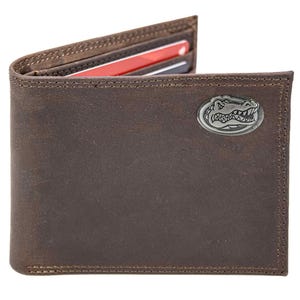 Puede incluir: Cartera de cuero marrón con un emblema de cocodrilo plateado. La cartera plegable tiene costuras visibles y contiene varias tarjetas de crédito. La cartera está hecha de cuero texturizado y envejecido.