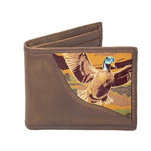Puede incluir: Cartera de cuero marrón con una imagen bordada detallada de un pato en vuelo. La cartera tiene un diseño plegable con ranuras para tarjetas y un compartimento para billetes. La imagen del pato presenta tonos marrones, azules y amarillos.
