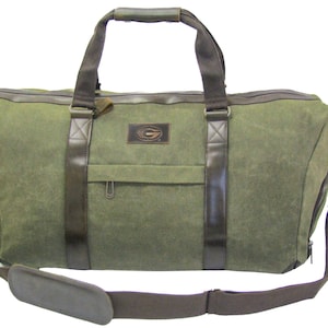 Könnte beinhalten: Eine grüne Canvas-Reisetasche mit braunen Lederelementen und einer Reißverschlusstasche auf der Vorderseite. Die Tasche hat einen oberen Griff und einen abnehmbaren Schultergurt.