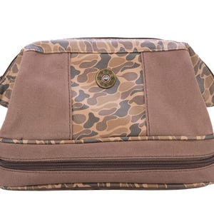 May include: A brown and tan camouflage toiletry bag with a zipper closure and a brown handle. The bag has a small metal button on the front.