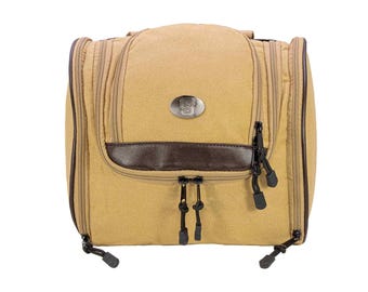 May include: Tan travel toiletry bag with multiple zippered compartments and a brown leather accent. The bag has a metal emblem on the front and black zipper pulls. The bag is designed for travel and personal care items.