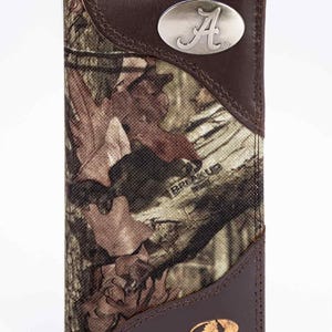 Puede incluir: Cartera con estampado de camuflaje con detalles en cuero marrón. Cuenta con un emblema ovalado plateado con la letra "A". La cartera tiene los logotipos "BREAK UP INFINITY" y "MOSSY OAK".