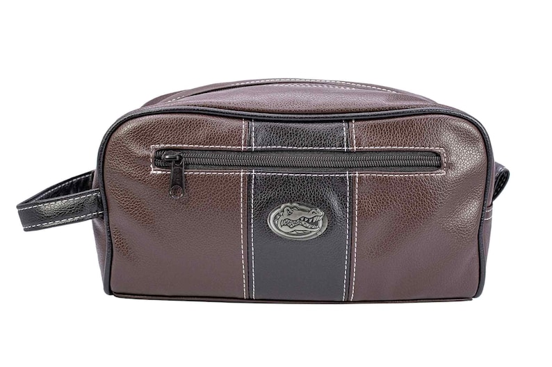 Puede incluir: Neceser de cuero marr&oacute;n y negro con cierre de cremallera y asa. La bolsa presenta una franja negra en el centro con un emblema plateado y costuras blancas. La bolsa es rectangular.