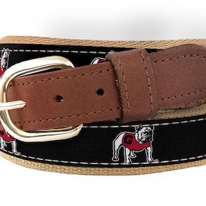May include: A brown leather belt with a gold buckle. The belt has a black and tan striped pattern with a repeated image of a white bulldog wearing a red jersey with a white "G" on it.