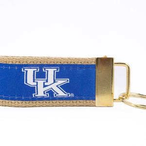 May include: A blue and tan key chain with a gold key ring and a white "UK" logo.