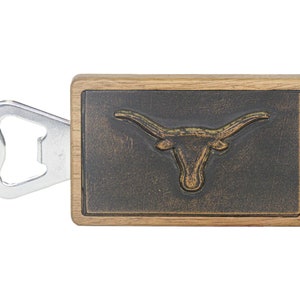 May include: Wooden bottle opener with a metal bottle opener attached. The wooden part has a black background with a gold embossed Longhorn steer head.