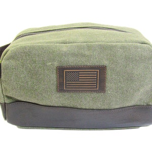 Peut inclure: Trousse de toilette en toile vert olive avec une base et une poignée en cuir marron. Comprend un patch en cuir marron avec un drapeau américain gravé. Le sac a une fermeture éclair et est conçu pour les voyages.