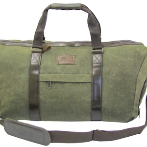 Könnte beinhalten: Olivgrüne Canvas-Reisetasche mit braunen Lederakzenten. Mit einem oberen Griff, Schultergurt und einer kleinen Vordertasche. Enthält einen braunen Lederaufnäher mit einer amerikanischen Flagge.