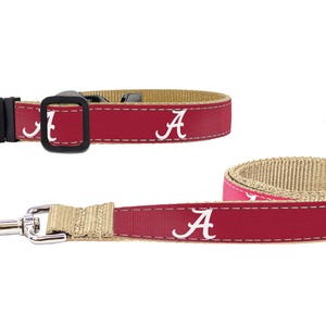 May include: A dog collar and leash set. The collar and leash are crimson red with the white letter "A" repeated across the length. The leash has a silver metal clasp and a tan-colored interior.