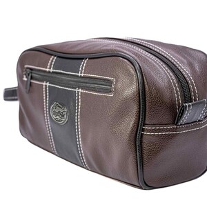 Puede incluir: Neceser de cuero marr&oacute;n con un dise&ntilde;o de rayas negras y blancas. Cuenta con cierre de cremallera, costuras blancas y un peque&ntilde;o logotipo. La bolsa tiene un asa lateral.