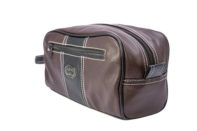 Puede incluir: Neceser de cuero marr&oacute;n con un dise&ntilde;o de rayas negras y blancas. Cuenta con cierre de cremallera, costuras blancas y un peque&ntilde;o logotipo. La bolsa tiene un asa lateral.