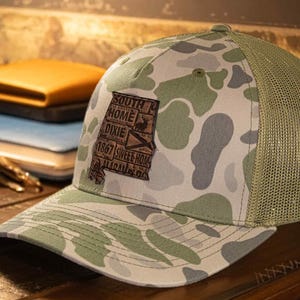 Alabama karta Old School kamouflage truckerkeps. Polerat fullnarvat lädermärke. Richardson 112 Snapback-keps med 5 paneler. Sytt kartmärke.