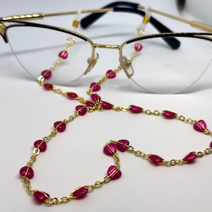 A pair of glasses with a golden chain with pink heart beads in a shape of a heart.