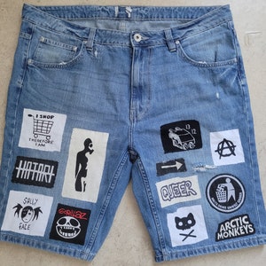 May include: Blue denim shorts with various patches, including "I Shop Therefore I Am", "Gorillaz", "Sally Face", "Arctic Monkeys", "Queer", and an anarchy symbol.
