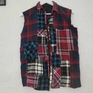 May include: A sleeveless patchwork vest with a button-up front. The vest is made of different plaid fabrics in shades of red, blue, and green.