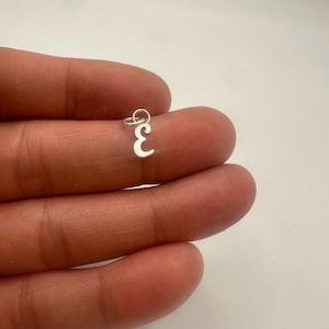 Peut inclure: Un petit pendentif en métal argenté en forme de chiffre trois. Ce bijou présente une surface lisse et réfléchissante et comprend un anneau de jonction circulaire sur le dessus pour la fixation, présenté comme un composant de bijouterie.