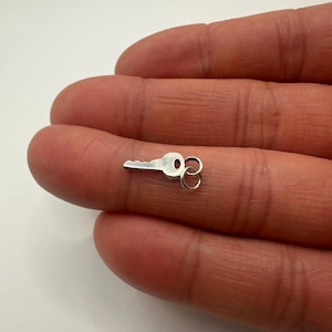 May include: A small, silver-colored key with a classic keyhole design. The key has a rounded bow and a single, small loop. The key is shown against a neutral background.