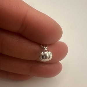 Può includere: Un piccolo ciondolo color argento lucido a forma di zucca in miniatura. Il ciondolo presenta scanalature verticali e un piccolo anellino circolare fissato sulla parte superiore, progettato per essere usato come pendente o decorazione.