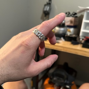 May include: A silver chain link ring with a thick band.