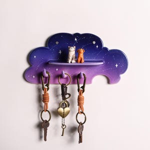 May include: A cloud-shaped key holder with a gradient purple and blue finish, featuring a shelf with cat and dog figurines. Three keychains hang below. The key holder has a starry night design.